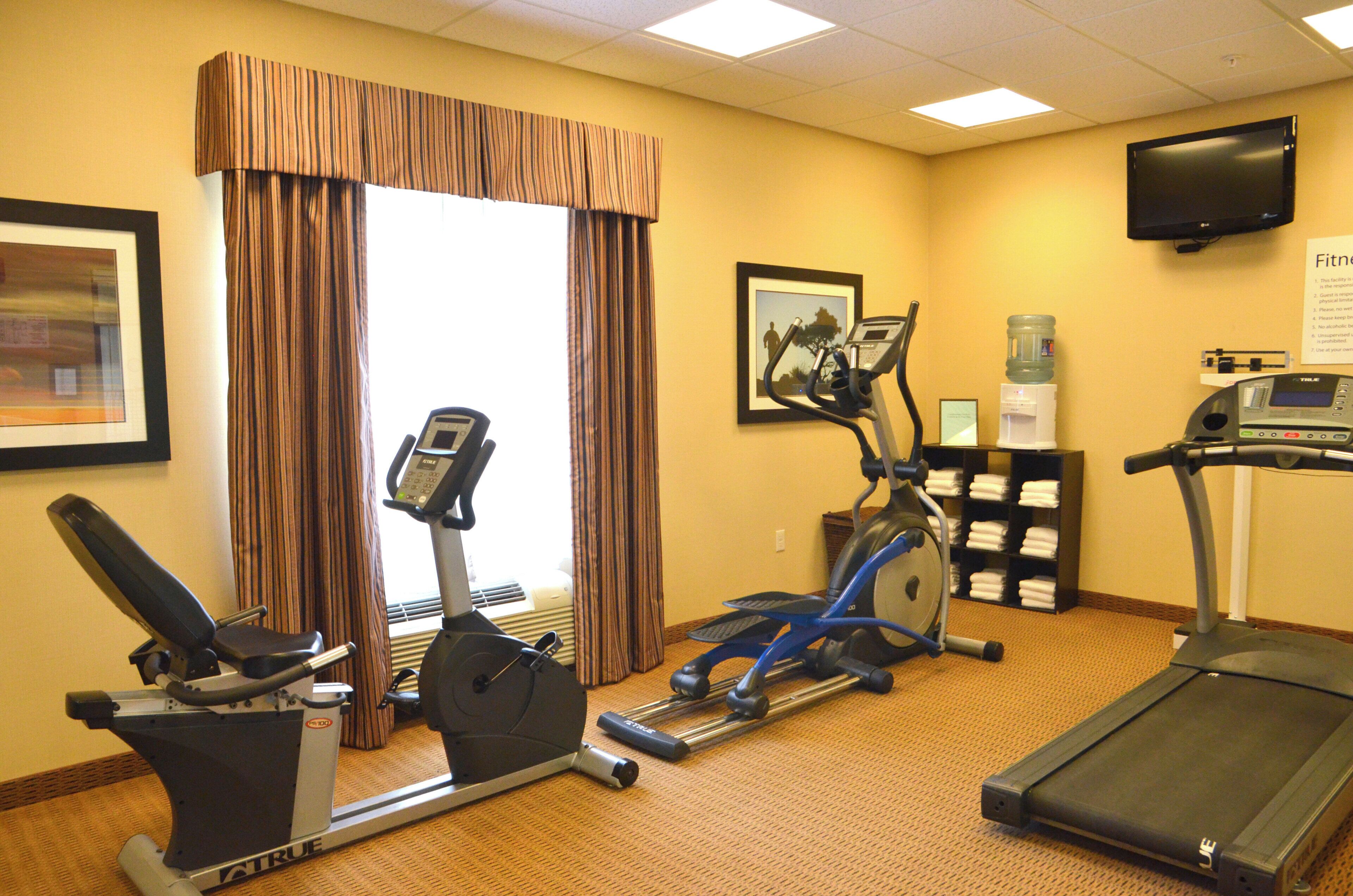 A hotel fitness room with exercise equipment, a television, and a water dispenser.