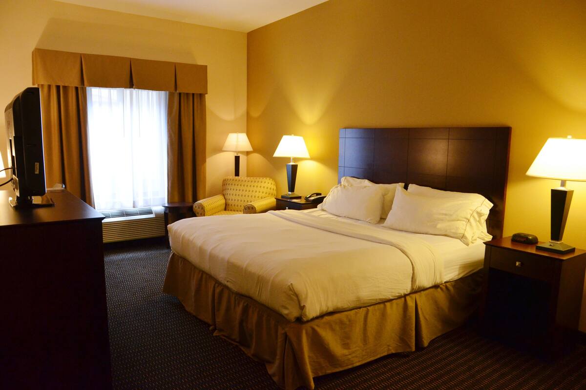 A hotel room with a large bed, two bedside lamps, a chair, and a desk with a lamp.
