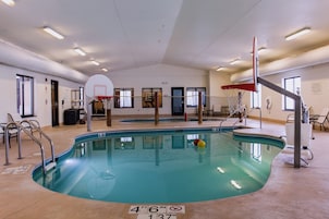Una piscina interior con aro de baloncesto, sillas junto a la piscina y puesto de socorrista.