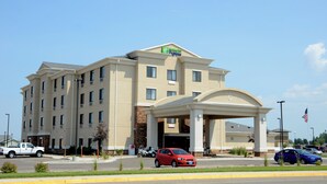 Un hotel Holiday Inn Express con un ingresso centrale, diversi piani e un parcheggio con vari veicoli.