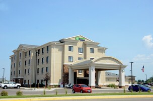 Un hotel Holiday Inn Express con entrada central, varios pisos y un estacionamiento con diferentes vehículos.