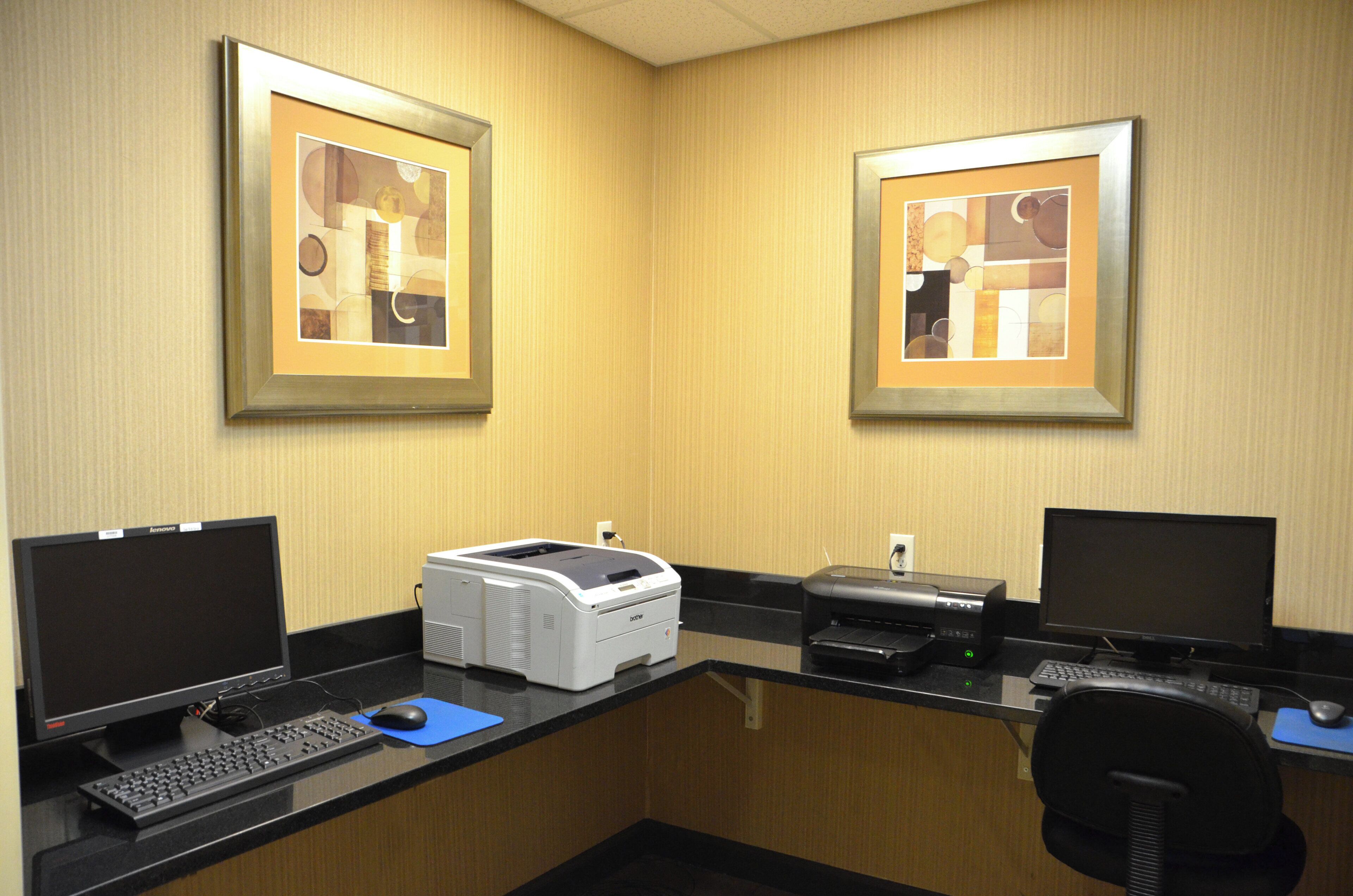 Ein Hotelbüro mit zwei Schreibtischen, Computern, Druckern und gerahmten abstrakten Kunstwerken an der Wand.