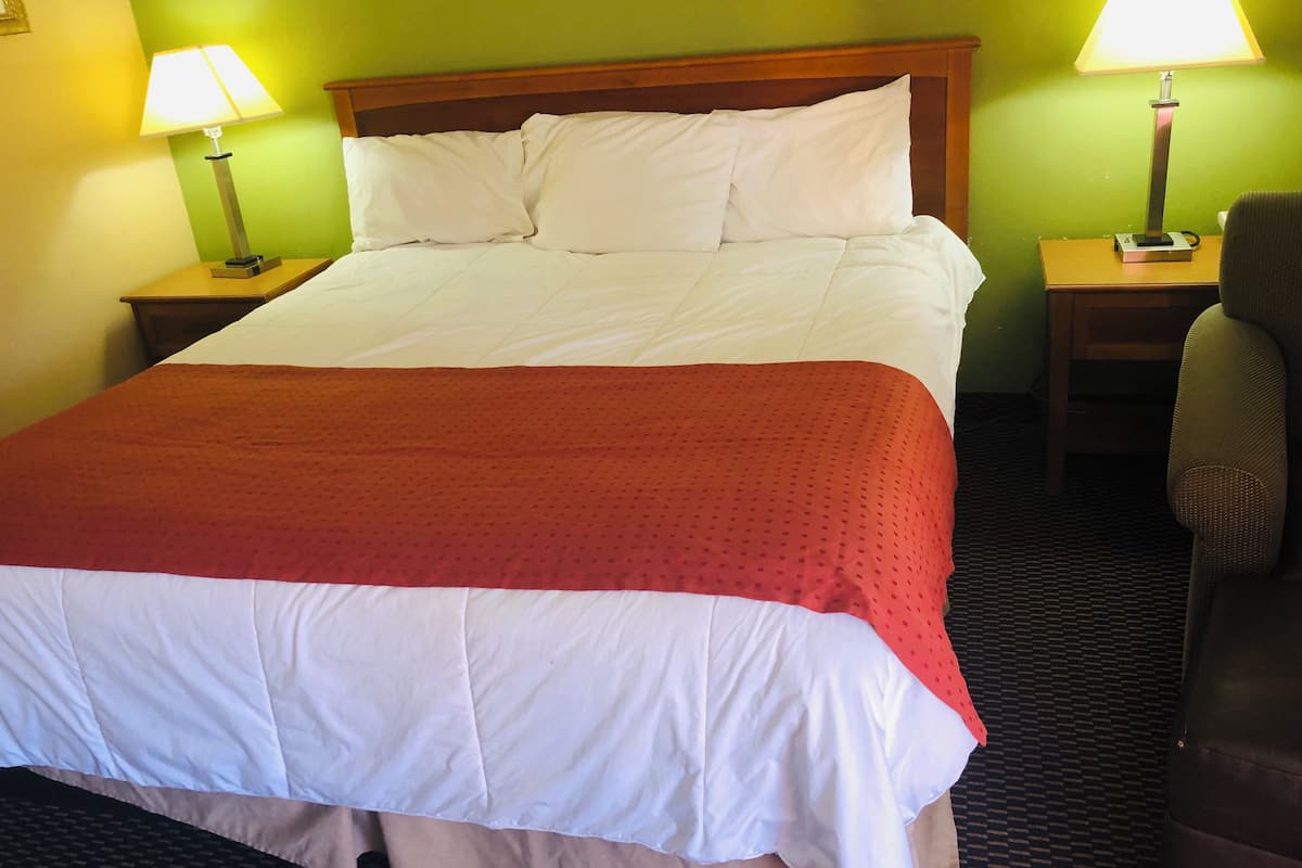 A hotel room with a large bed, two bedside tables with lamps, a chair, and green walls.
