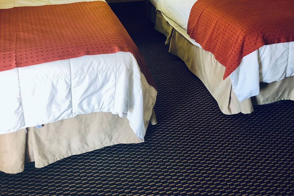 A hotel room with two beds, a nightstand with a lamp, and a framed artwork on the wall.