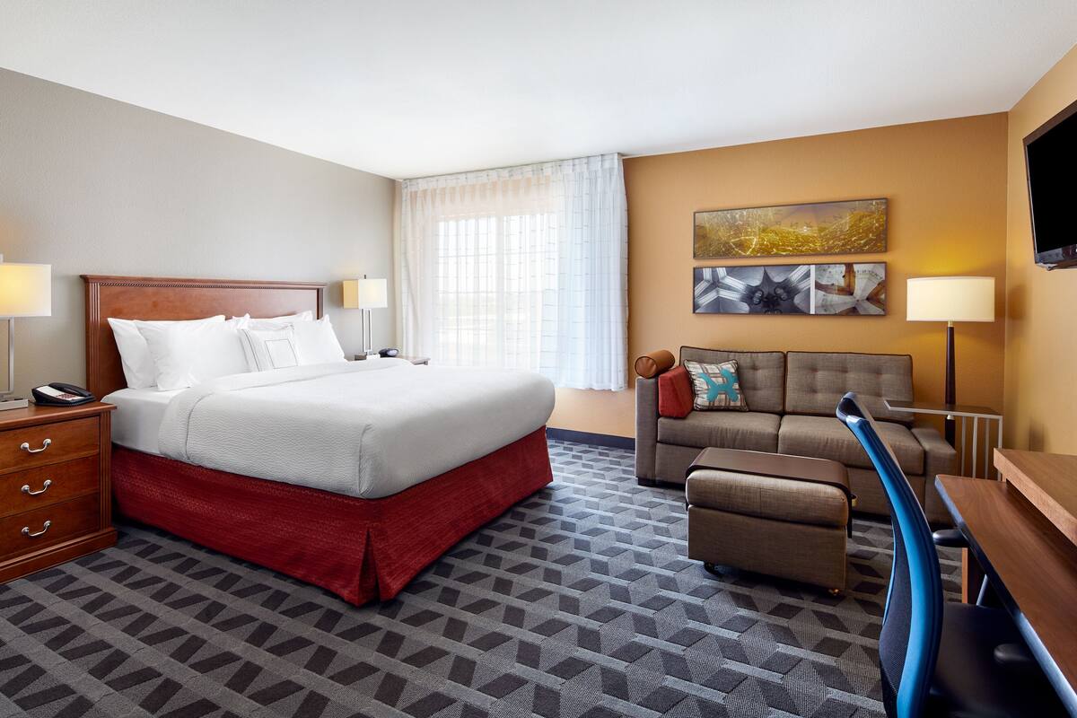 A hotel room with a large bed, a sofa, a desk, and a chair.