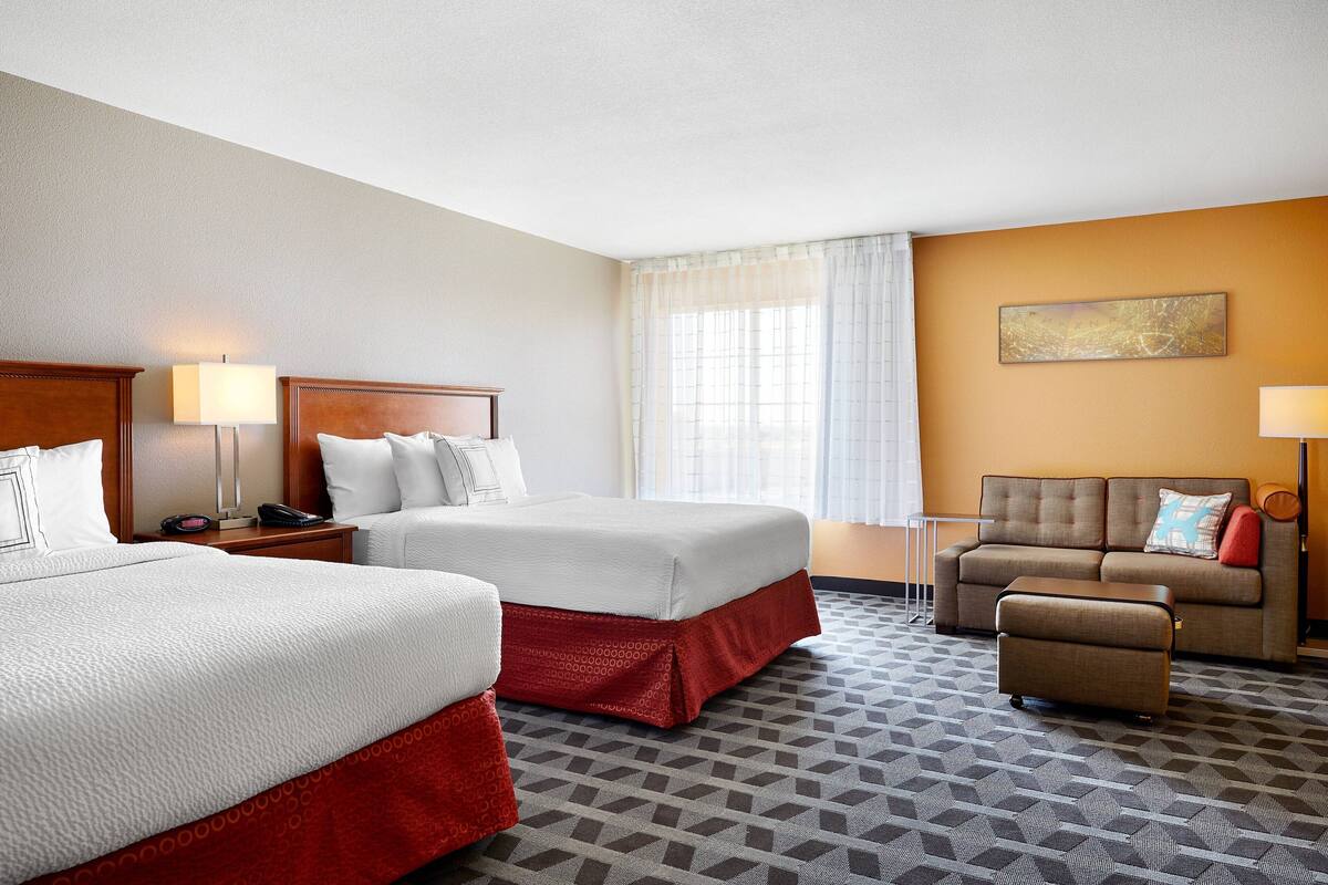 A hotel room with two beds, a sofa, and a small table.