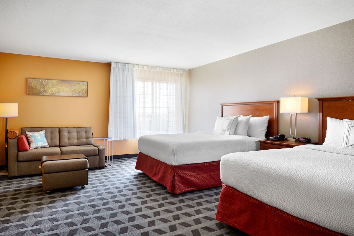 A hotel room with two beds, a sofa, a small table, and a lamp.