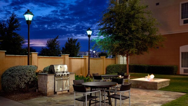 An outdoor patio with a grill, dining table, chairs, and a fire pit. - TownePlace Suites Midland (Midland)