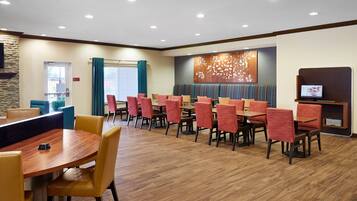 A hotel dining area with multiple tables and chairs, a television, and a stone wall.