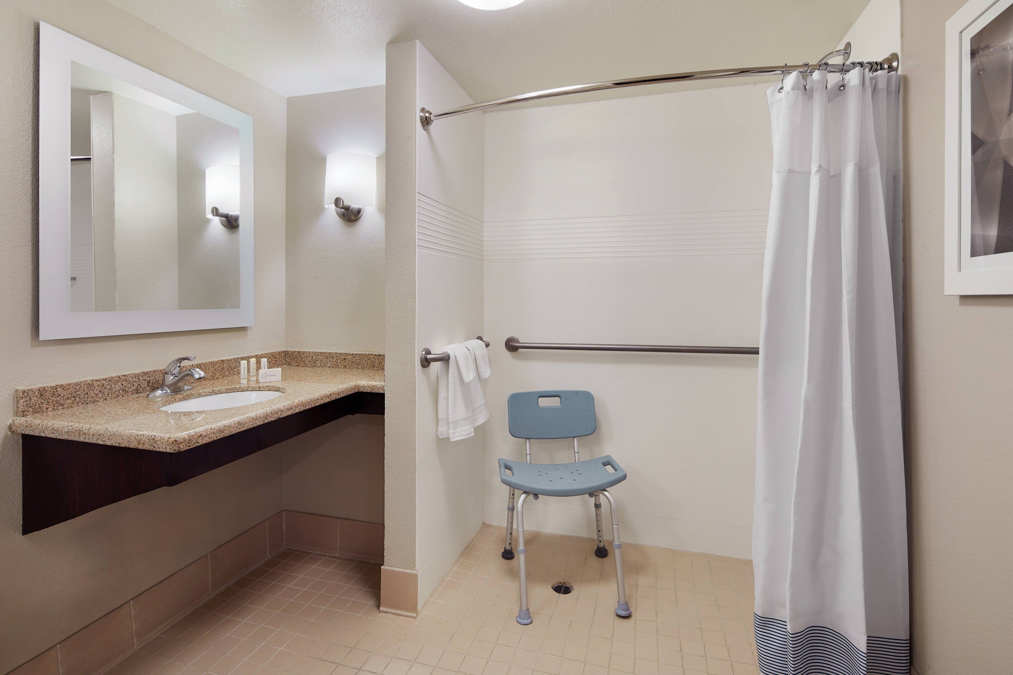 A bathroom with a sink, mirror, shower, and a wheelchair.