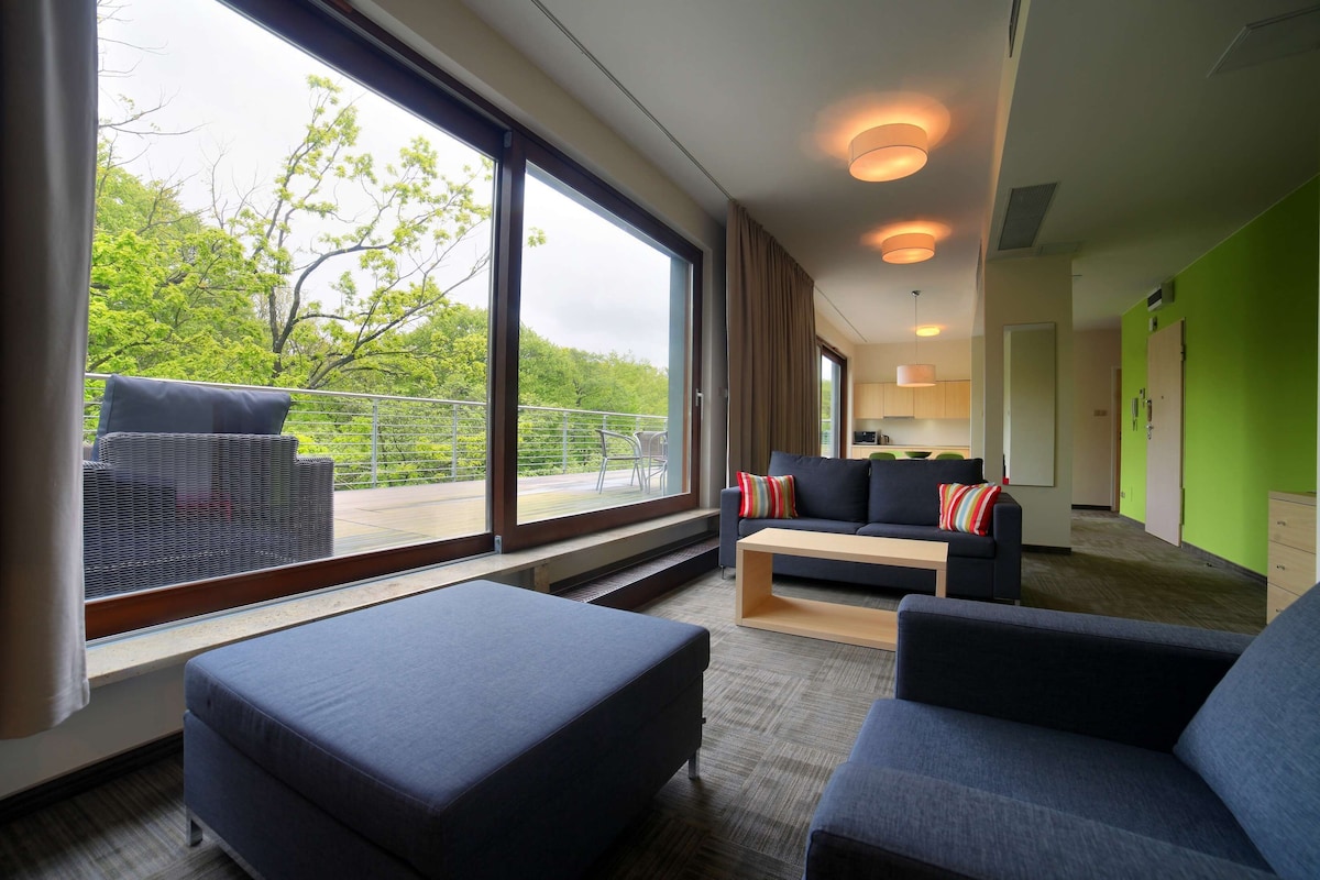 Ein modernes Hotelzimmer mit großem Fenster, Balkon, Sofa, Couchtisch und Bett.