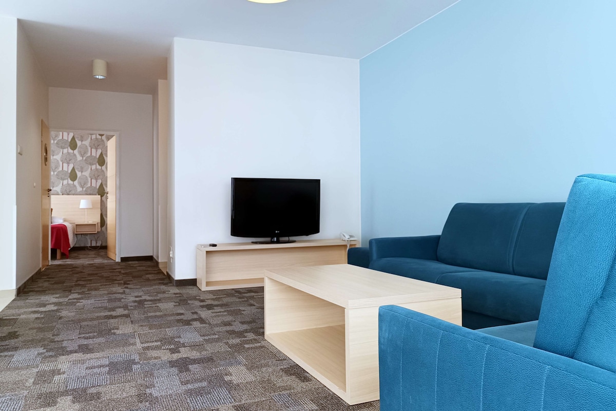 Ein modernes Wohnzimmer mit einem Flachbildfernseher auf einem Holztisch, einem blauen Sofa, einem Holztisch und einem gemusterten Teppich.