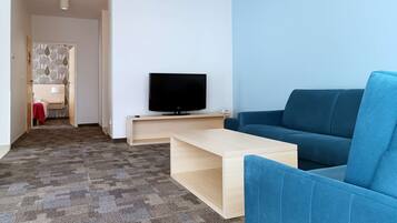 A modern living room with a flat-screen TV on a wooden stand, a blue sofa, a wooden coffee table, and a patterned carpet.