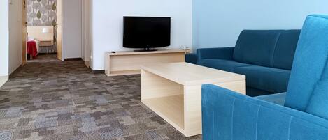 Una sala de estar moderna con un televisor de pantalla plana sobre un soporte de madera, un sofá azul, una mesa de centro de madera y una alfombra estampada.