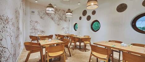 A modern dining area with wooden tables and chairs, hanging pendant lights, and decorative wall art.