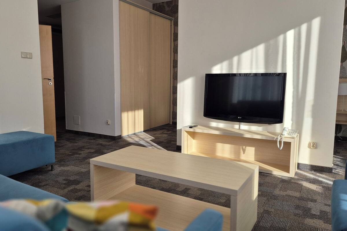 Un salon moderne doté d’un téléviseur à écran plat, de canapés bleus, d’une table basse en bois et d’une porte coulissante donnant sur une autre pièce.