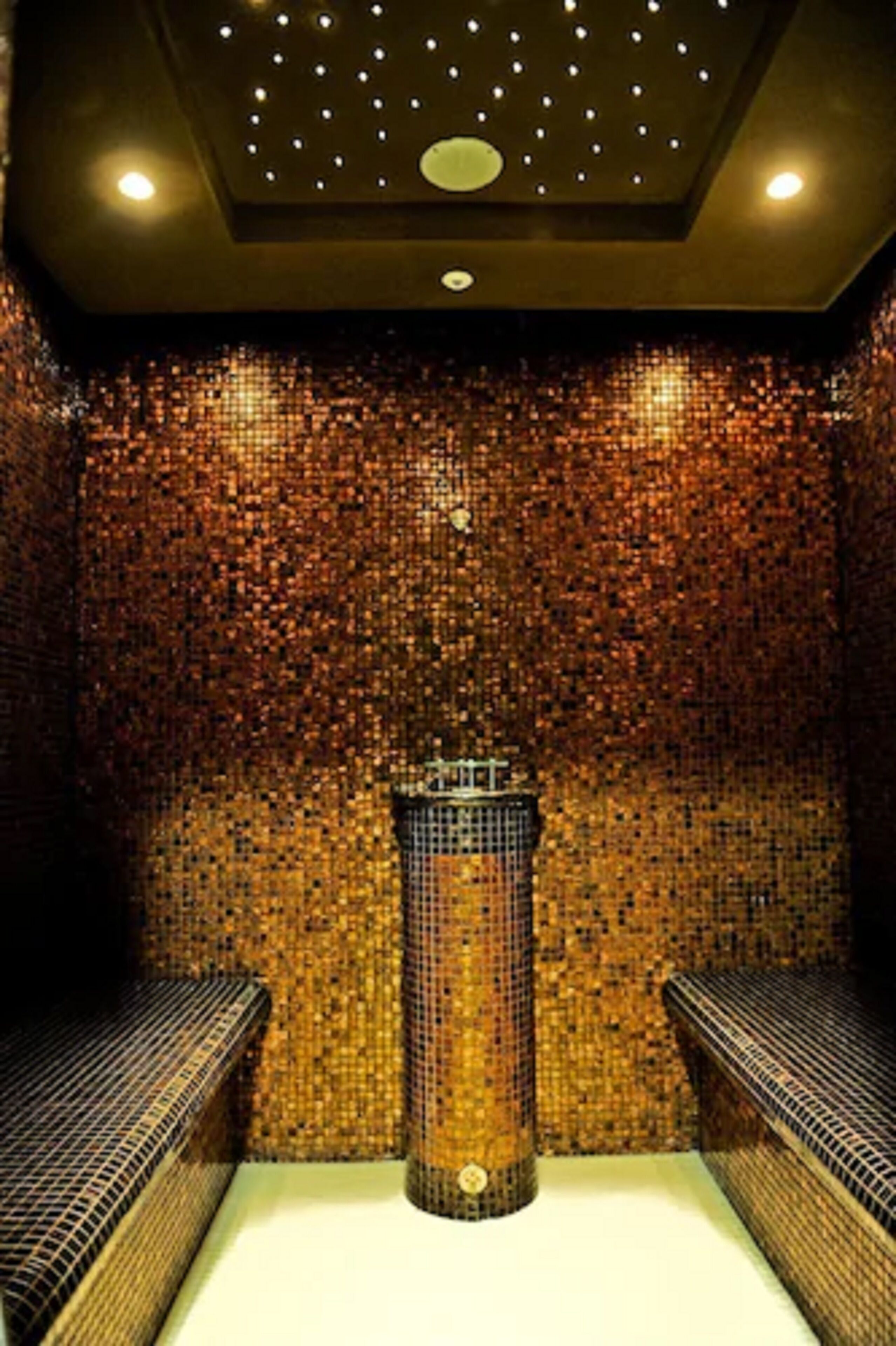 Et spa-rum med mosaikvægge, en central søjle og to bænke.
