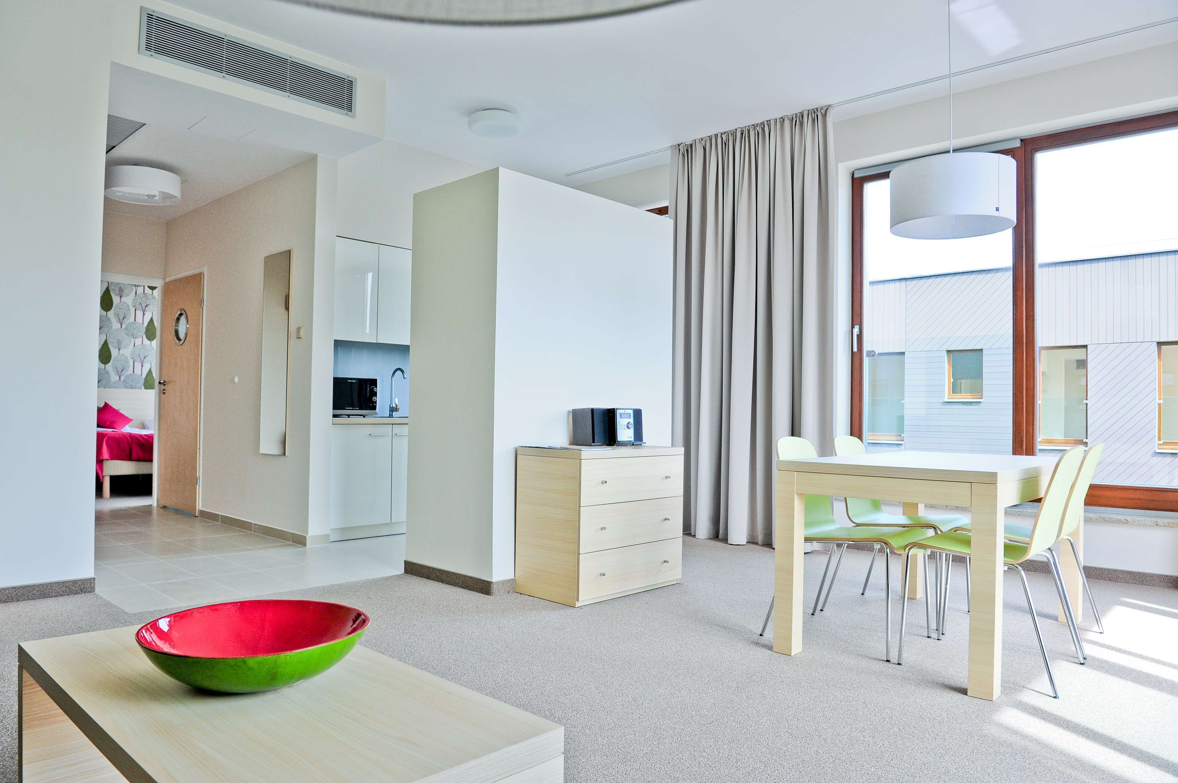 Een moderne hotelkamer met een eethoek, kitchenette en een groot raam met gordijnen.