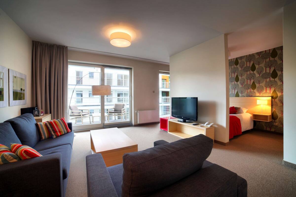 Une chambre d’hôtel moderne dotée d’un canapé, d’une télévision, d’une table à manger et d’un balcon offrant une vue sur la ville.