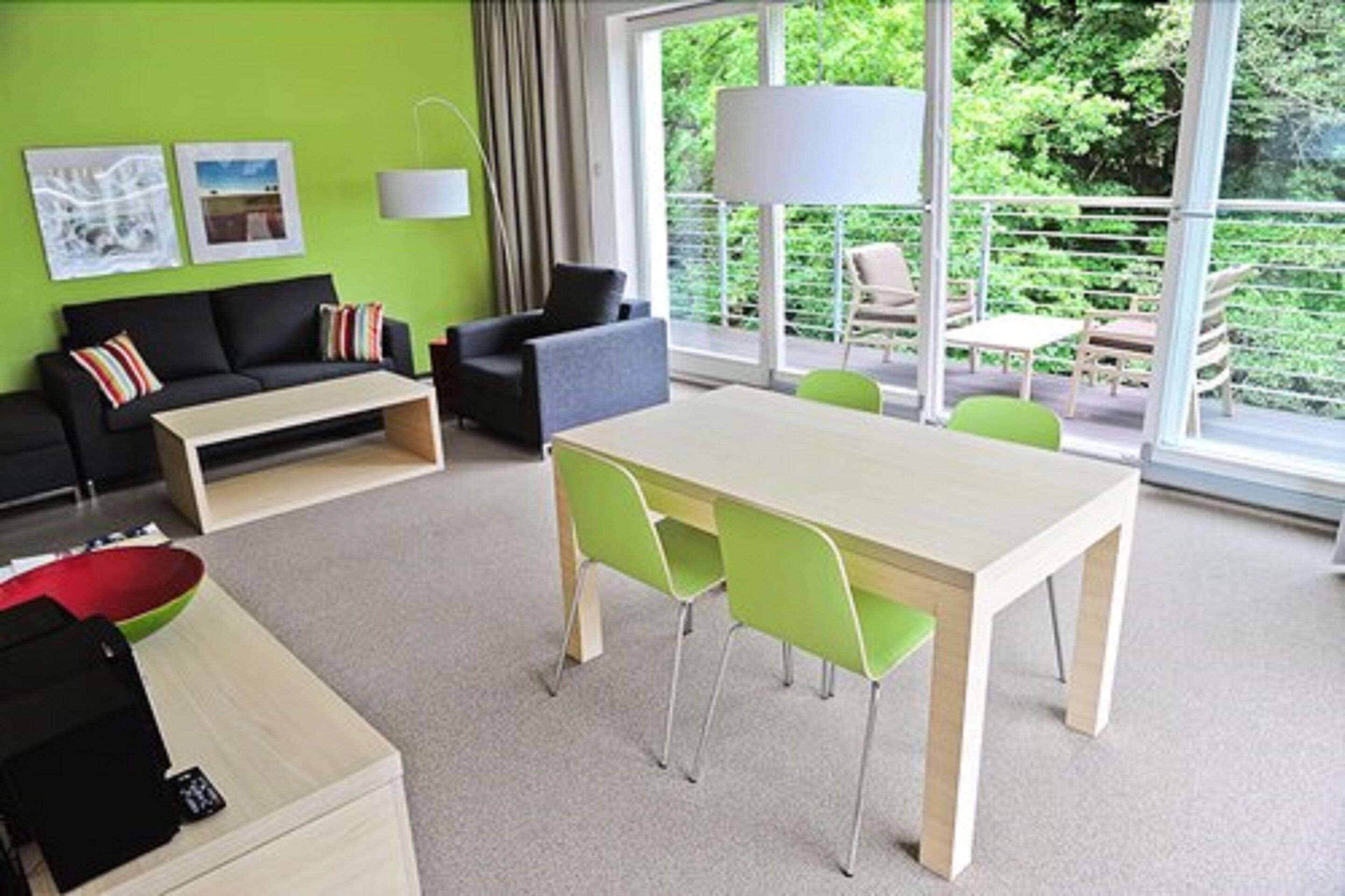 Ein modernes Wohnzimmer mit grüner Wand, einer Couch, einem Couchtisch, einem Esstisch mit Stühlen und einem Balkon mit Sitzgelegenheiten.