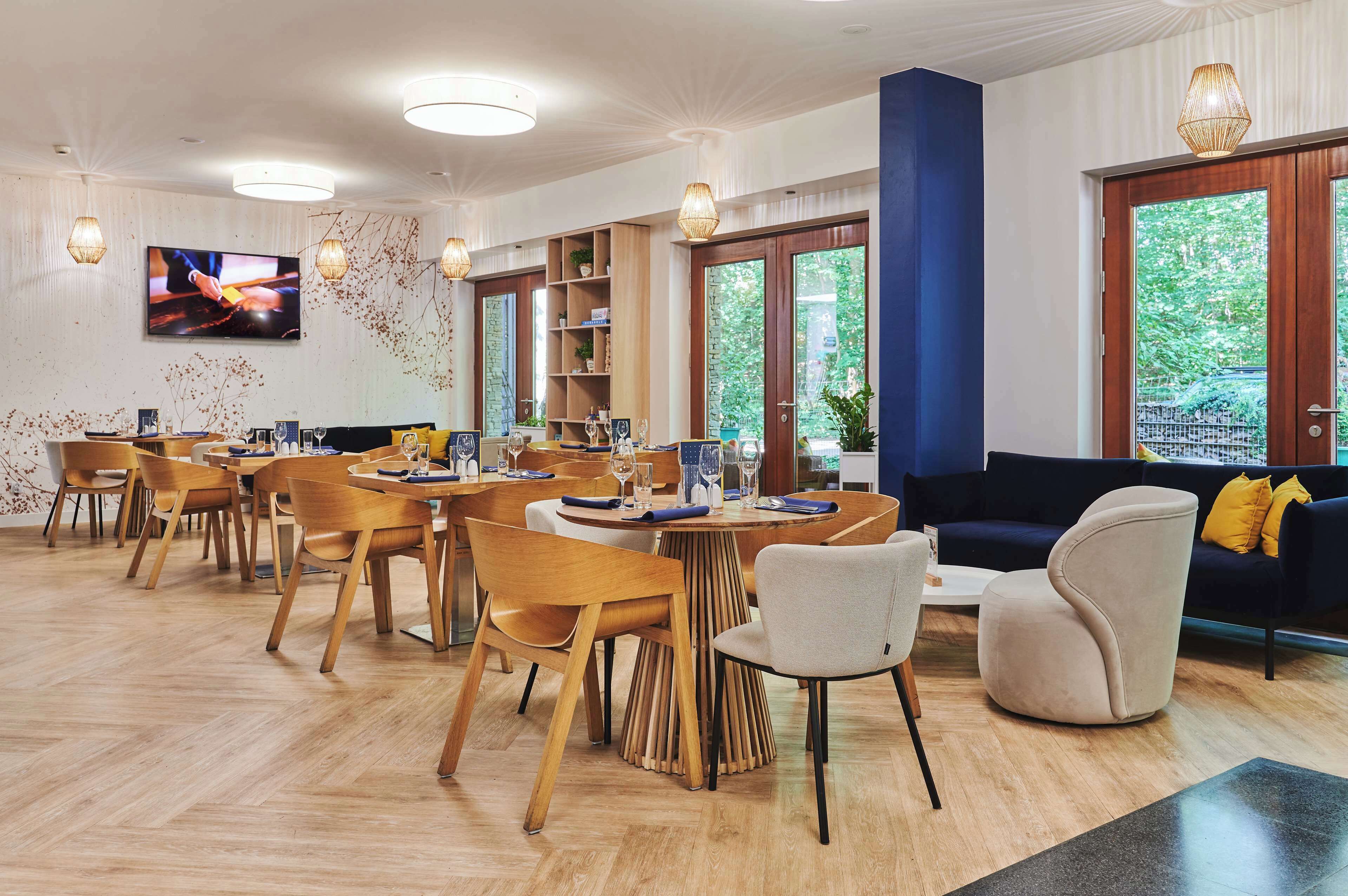 A modern dining area with wooden tables and chairs, a sofa, and a TV screen.
