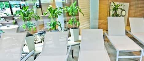 Una hall d'hotel moderna con poltrone bianche, piante in vaso e un divisorio in vetro.