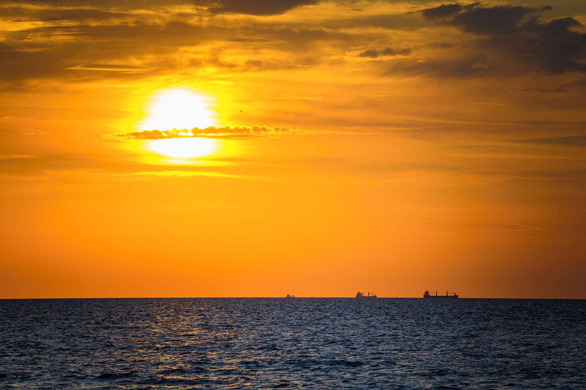 A sunset over the ocean with ships in the distance.