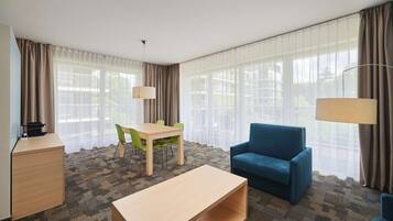 Une chambre d’hôtel équipée d’un bureau, d’un canapé bleu, d’une table à manger avec des chaises et de grandes fenêtres avec des rideaux.