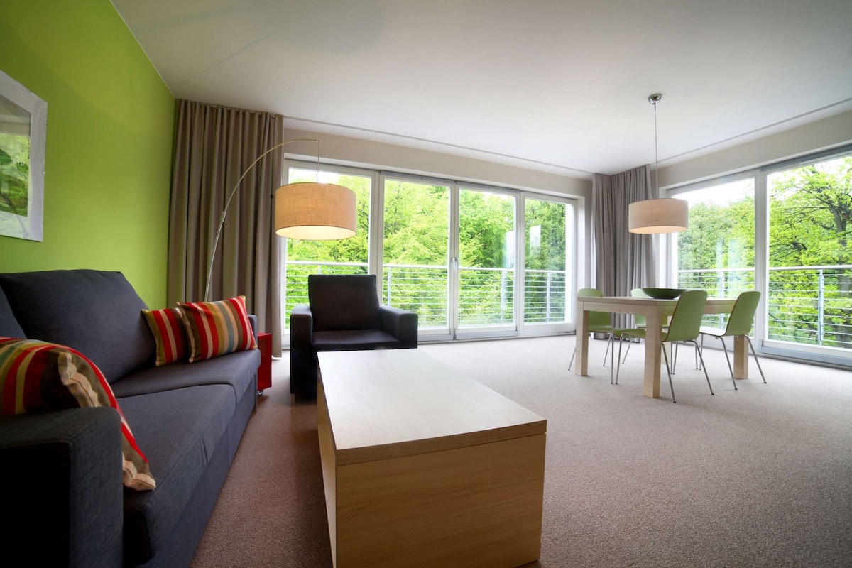 Ein modernes Wohnzimmer mit einer Couch, einem Couchtisch, einem Esstisch mit Stühlen, großen Fenstern und einem Balkon.