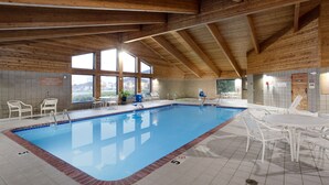 An indoor swimming pool with clear water, surrounded by white chairs and tables, and wooden beams on the ceiling. - AmericInn by Wyndham Plover Stevens Point (Plover)