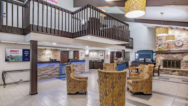 A spacious lobby with a high ceiling, a stone fireplace, and a reception desk. - AmericInn by Wyndham Plover Stevens Point (Plover)