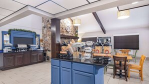 A kitchen with a central island, a stone accent wall, and a dining area with wooden chairs and tables. - AmericInn by Wyndham Plover Stevens Point (Plover)