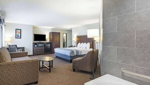 A hotel room with a bed, two armchairs, a small table, a TV, a microwave, and a bathroom with a bathtub. - AmericInn by Wyndham Plover Stevens Point (Plover)