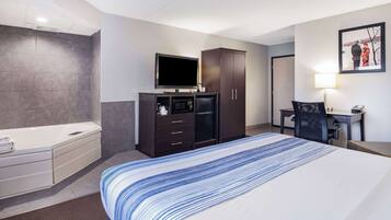 Ein Hotelzimmer mit einem großen Bett, einem Flachbildfernseher, einem dunklen Holzschrank, einem Schreibtisch mit Stuhl sowie einem Badezimmer mit Badewanne und Handtuchhalter.