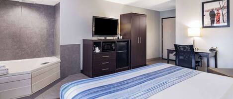 Habitación de hotel con una cama grande, un televisor de pantalla plana, un armario de madera oscura, un escritorio con silla y un baño con bañera y perchero.
