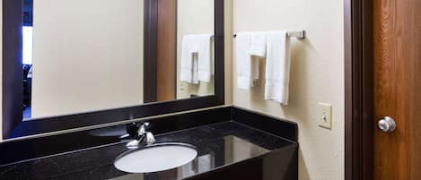 A bathroom with a black countertop sink, a large mirror, and a wooden door.