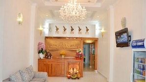A hotel reception area with a wooden counter, a chandelier, and a television screen displaying 'Cold Drinks'. - Green Centre Point Inn (Phnom Penh)