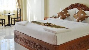 A neatly made bed with a wooden headboard, a small bedside table, and a chair. - Green Centre Point Inn (Phnom Penh)