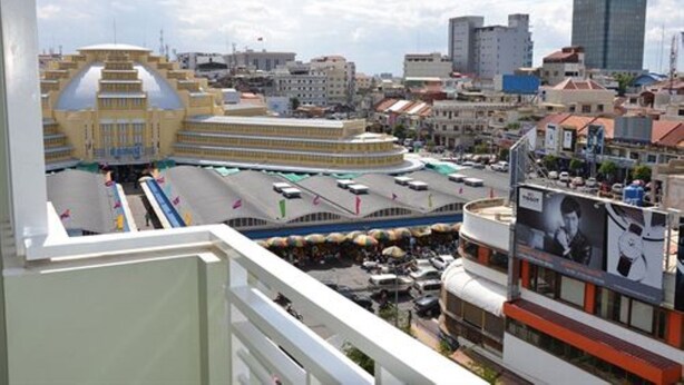 A cityscape with a prominent yellow building with a unique architectural design, a modern high-rise building, and a busy street with cars and pedestrians. - Green Centre Point Inn (Phnom Penh)