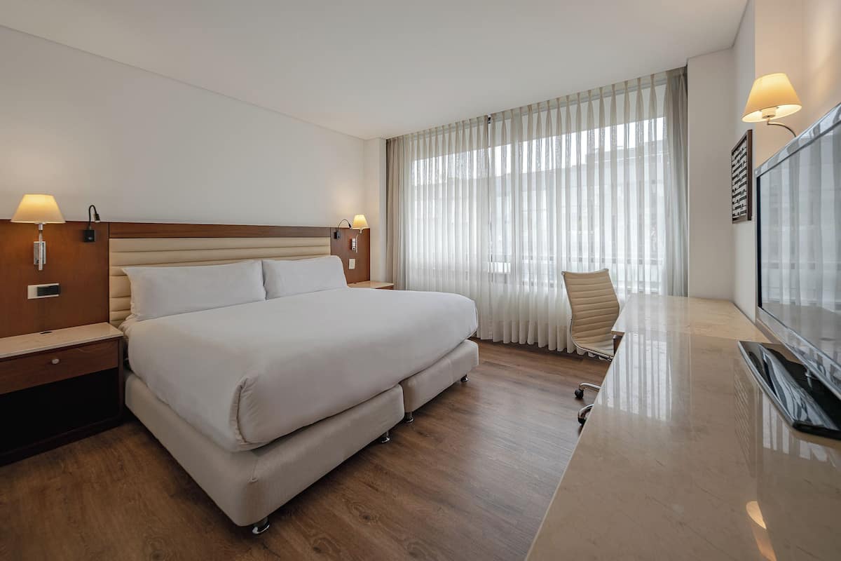 A hotel room with a large bed, a desk, a chair, and a TV.