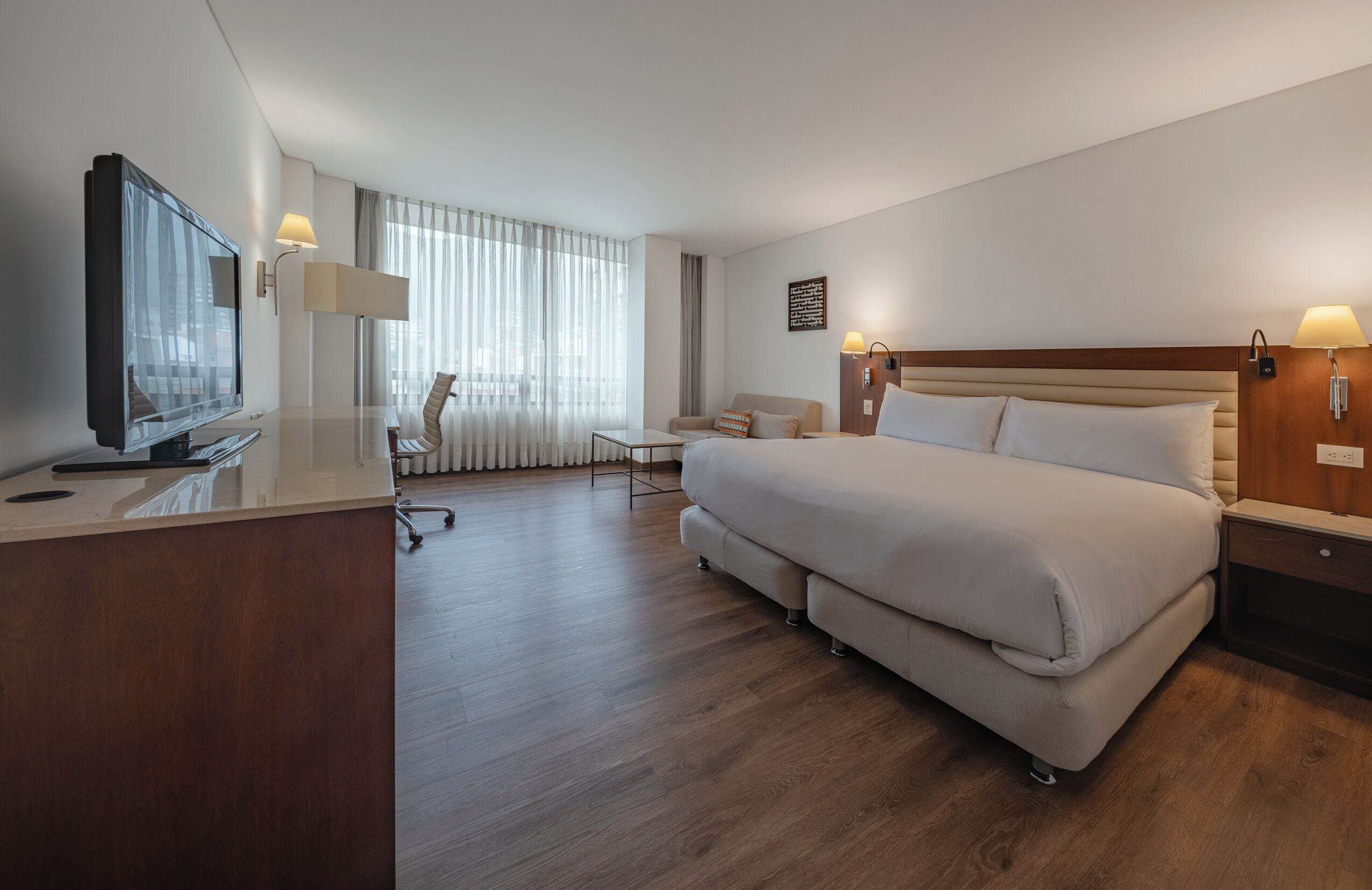 A hotel room with a large bed, a desk with a television, a chair, and a sofa.