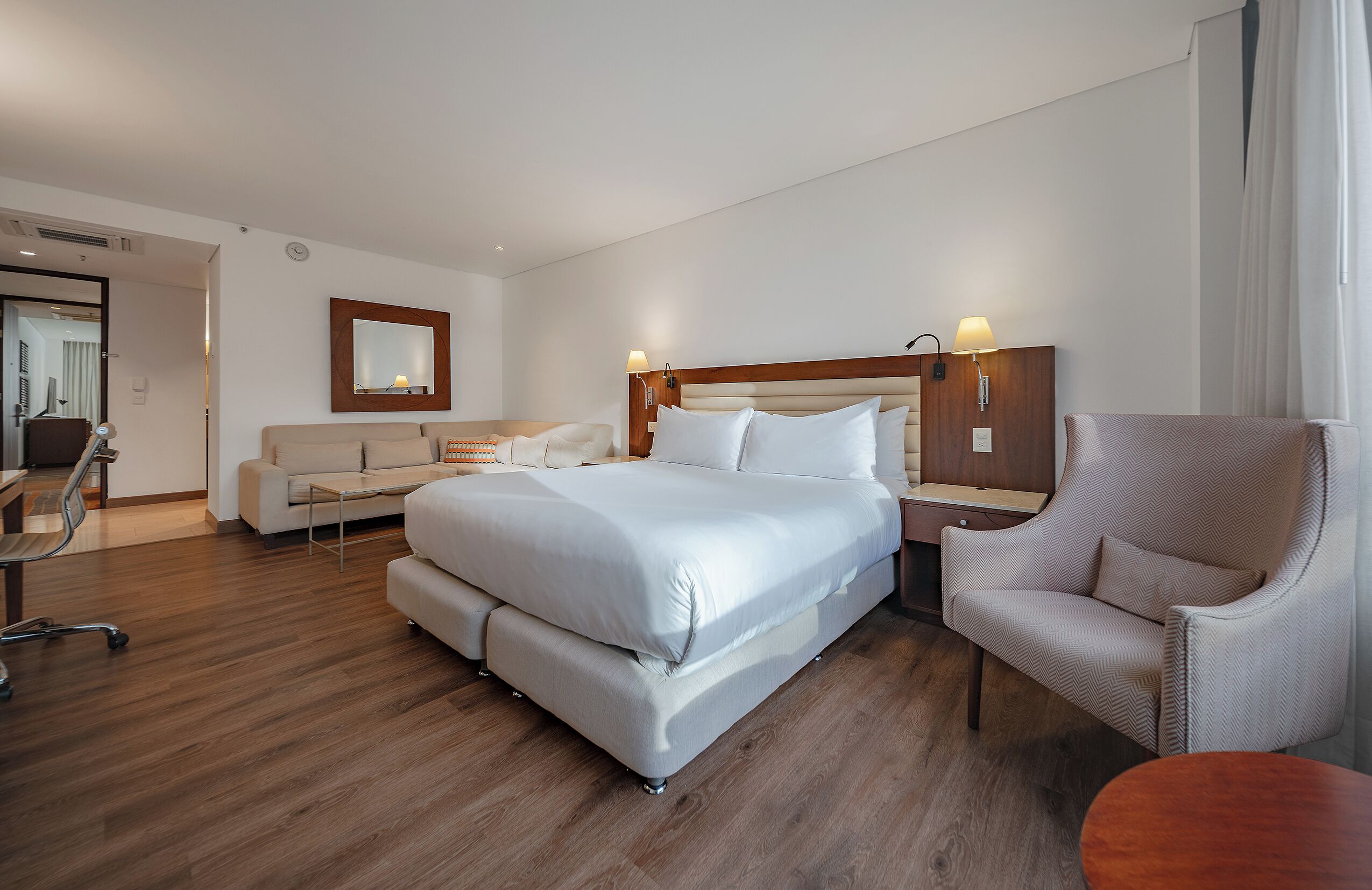 A hotel room with a large bed, a sofa, a chair, and a desk.
