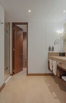 A modern bathroom with a wooden door, a beige tiled floor, a marble countertop, and a large mirror.