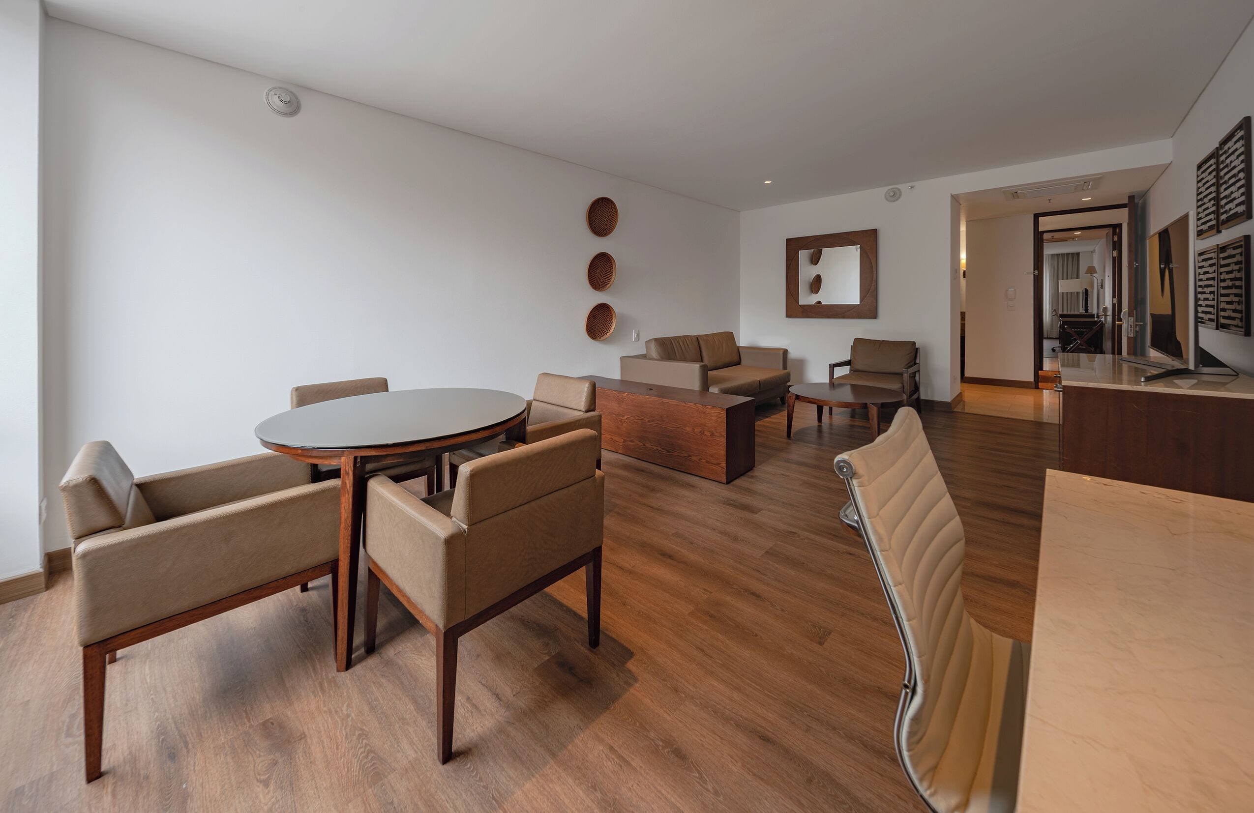 A modern living room with a round dining table, sofas, and a kitchen area visible through an open doorway.