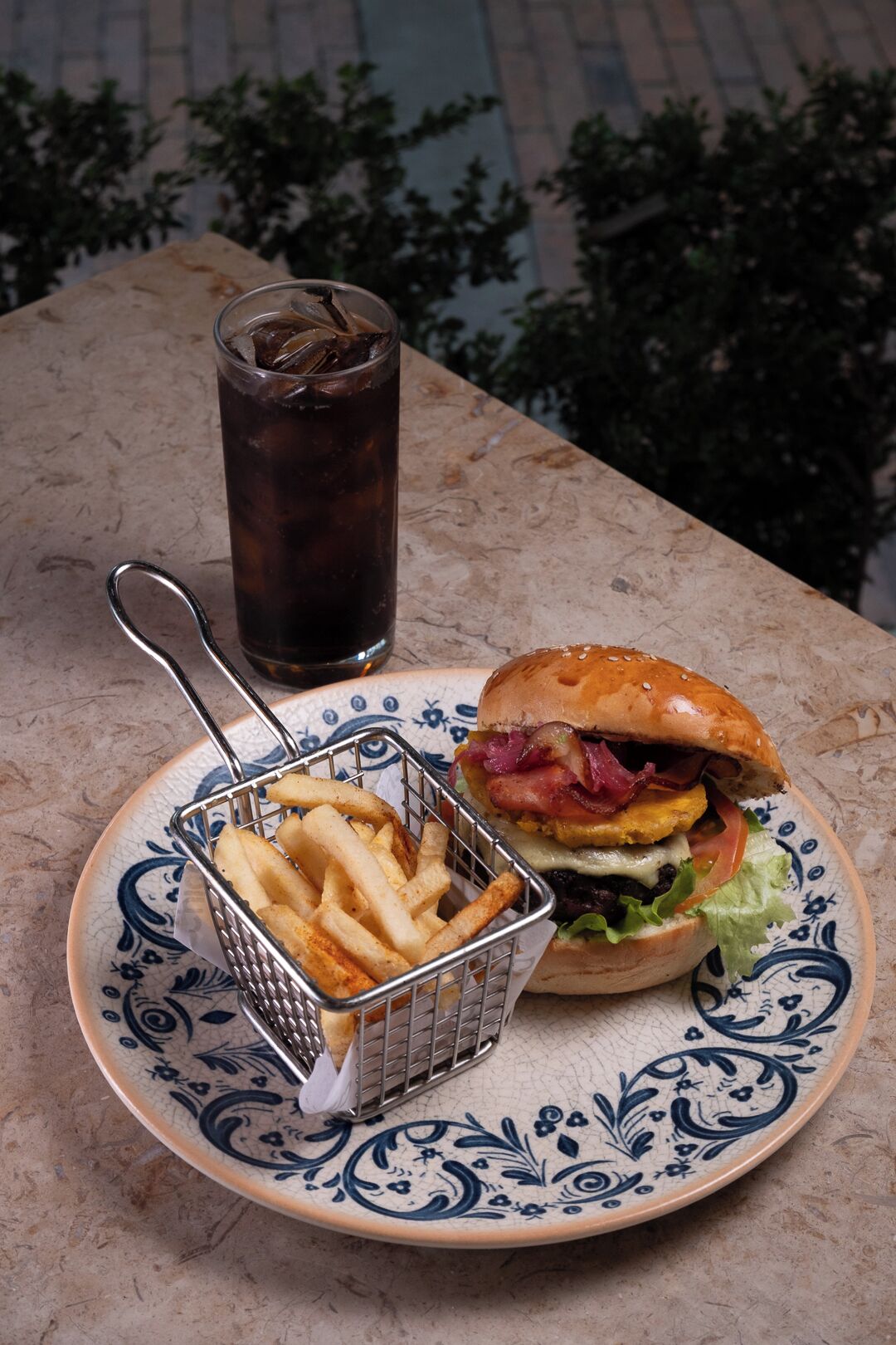 A plate with a burger and fries, a glass of iced drink, and a decorative plate.