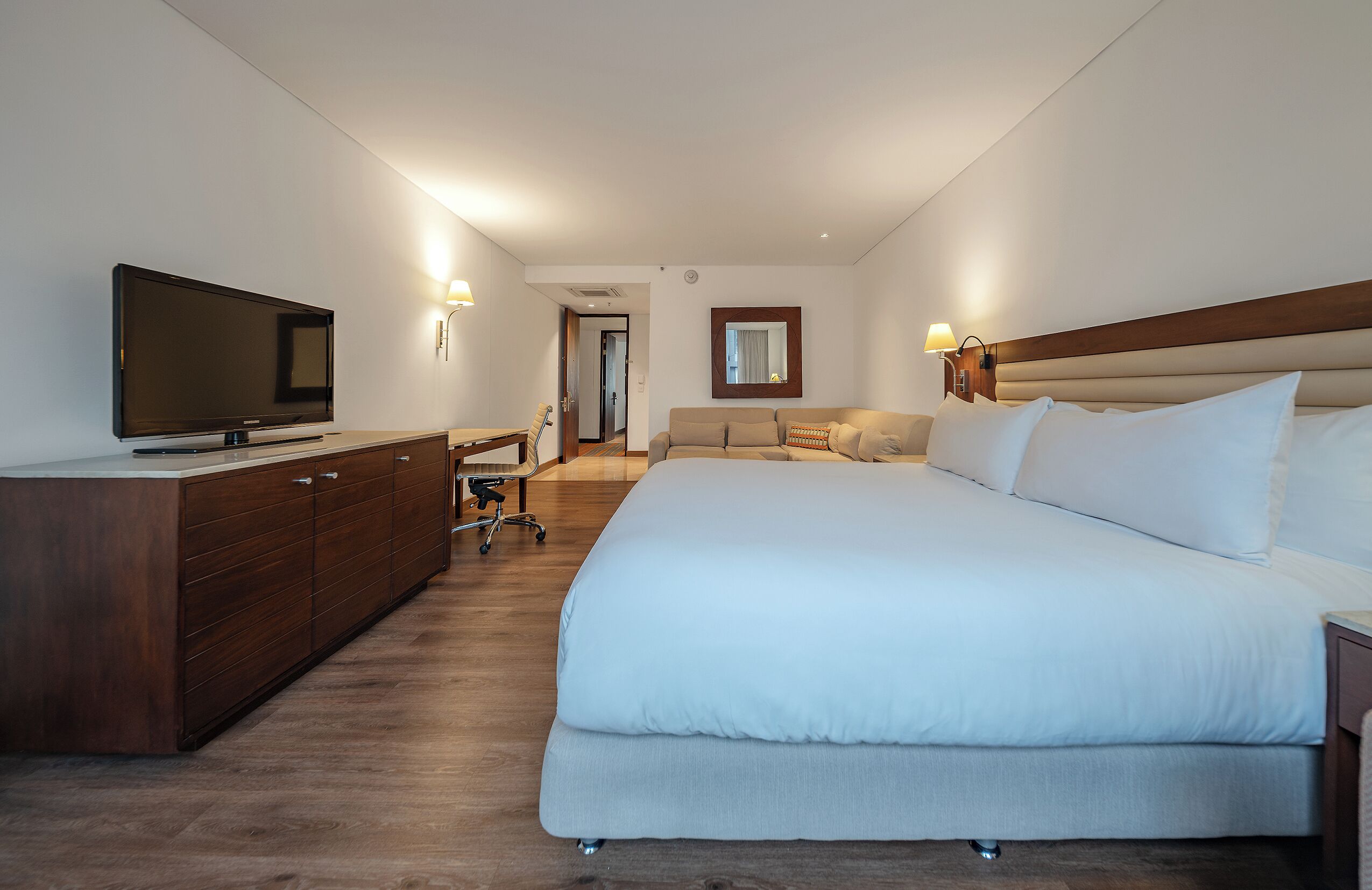 A hotel room with a large bed, a TV, a desk, and a chair.