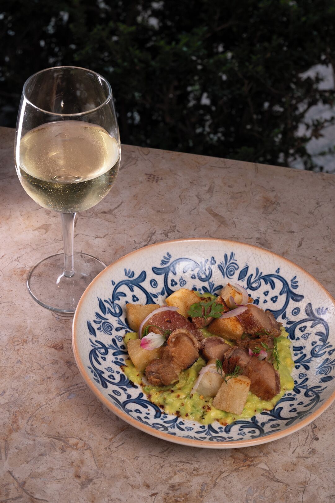 A plate of food with a glass of white wine on a table.