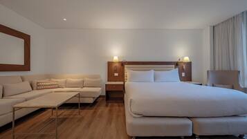 A modern hotel room with a large bed, a sofa, a small table, and a chair.