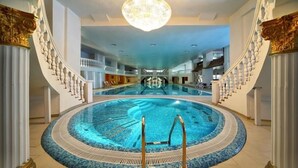 Una amplia piscina interior con una zona de buceo central, rodeada por un solárium alicatado y una escalera en un lateral.