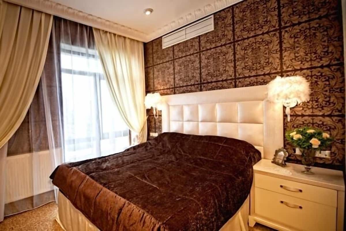 A bedroom with a large bed, a nightstand with a lamp, and a decorative wall panel.